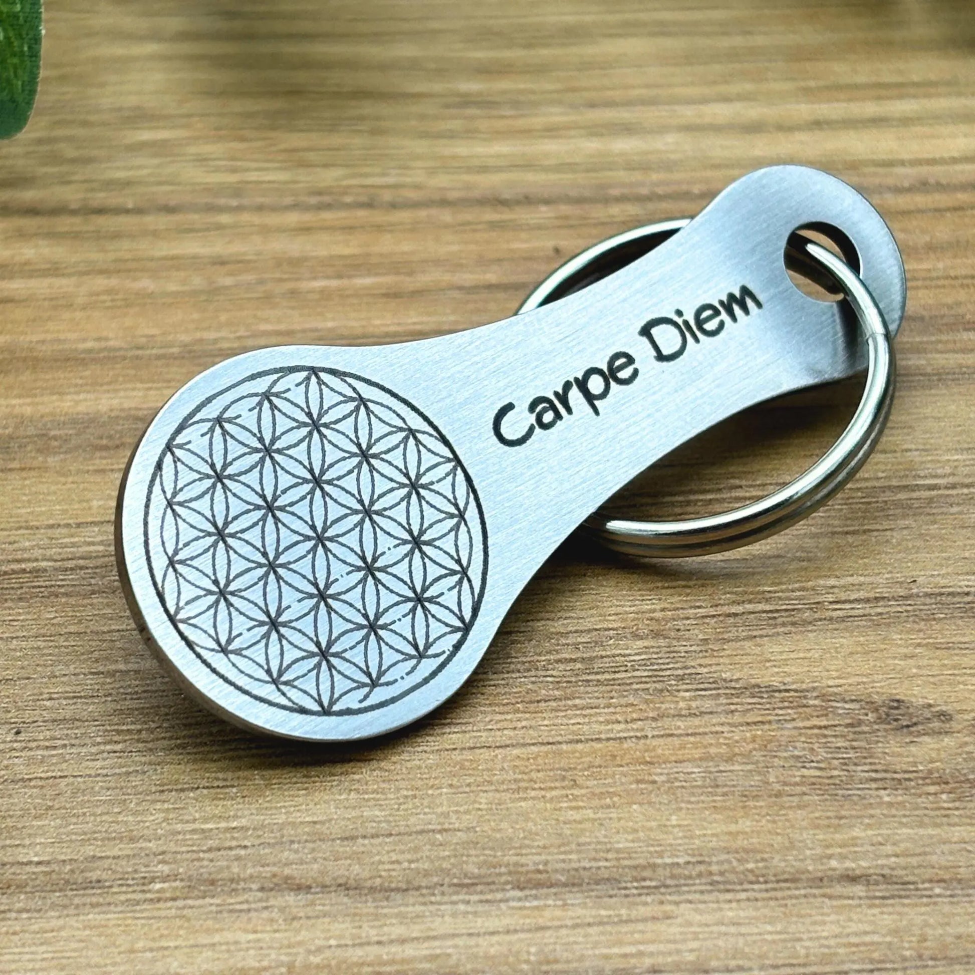Hochwertiger Einkaufswagenchip aus Edelstahl mit Gravur "Carpe Diem" und Blume des Lebens, platziert auf Holzoberfläche