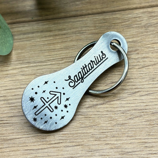 Edelstahl-Einkaufswagenlöser mit Sagittarius-Gravur – stilvoller Schlüsselanhänger mit Sternzeichen-Motiv auf Holzuntergrund.