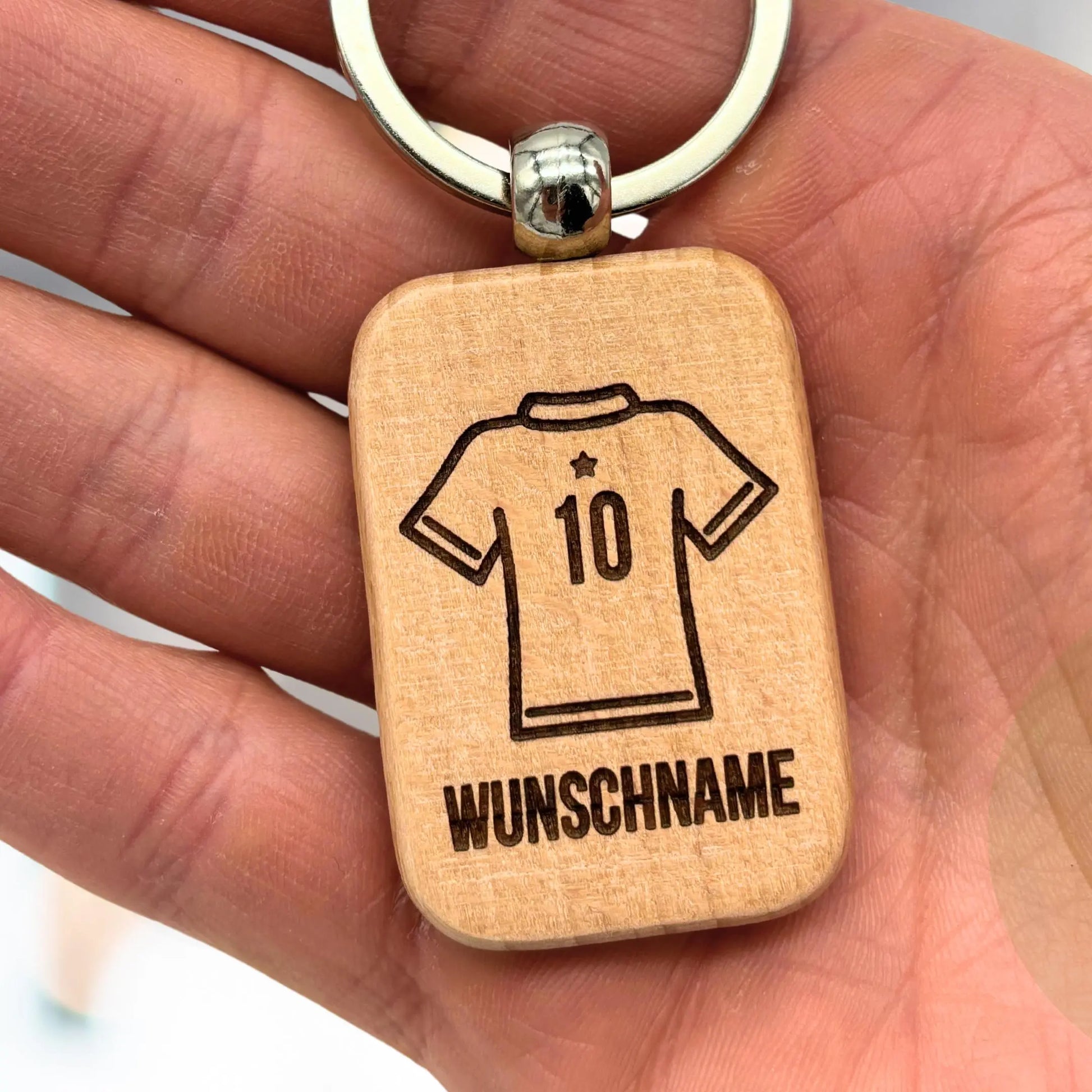 Hand hält personalisierten Holz-Schlüsselanhänger mit Gravur Trikot und Wunschname